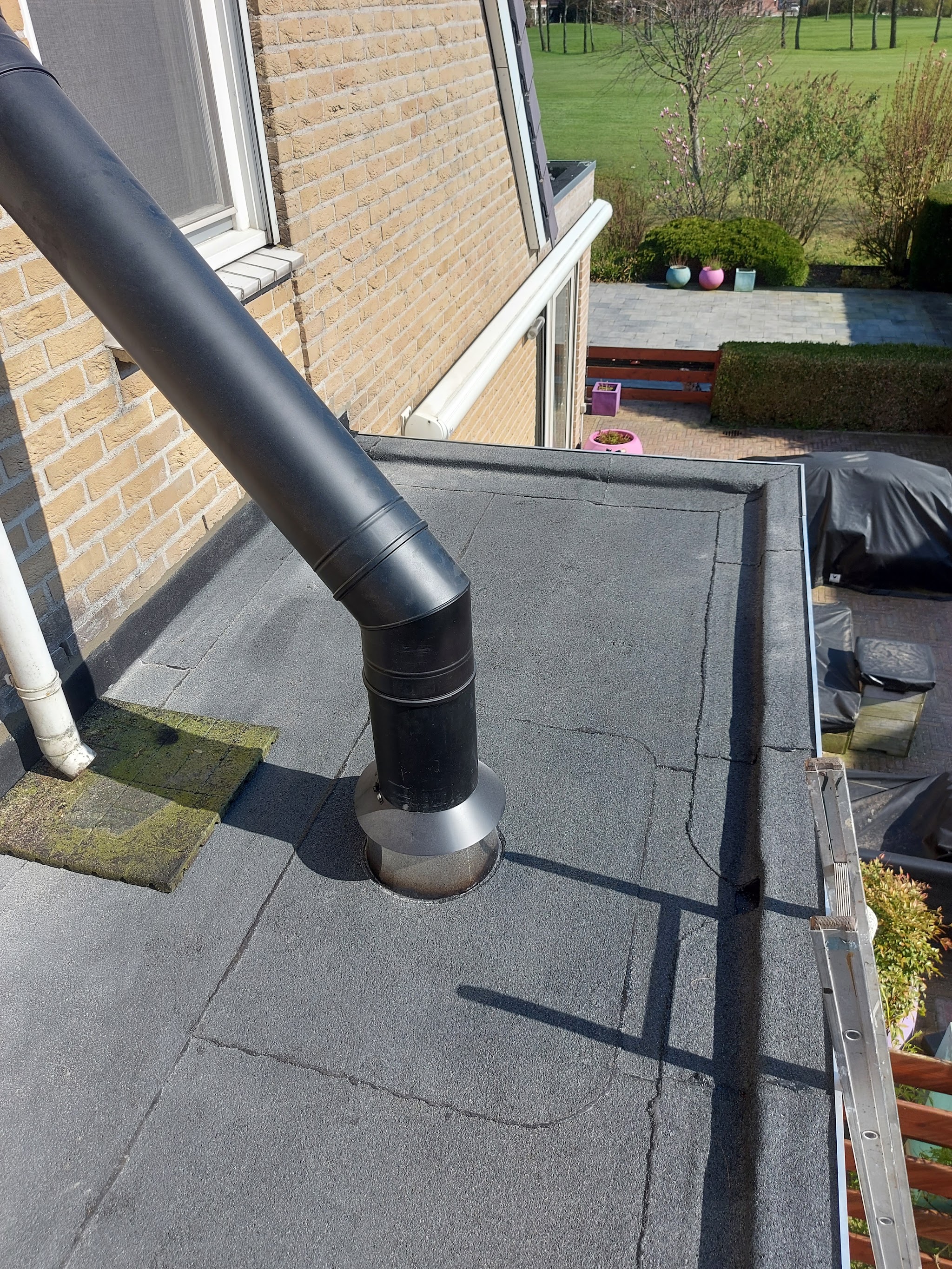 Plat dak met nieuwe bitumen dakbedekking en een zwarte afvoerpijp erdoorheen