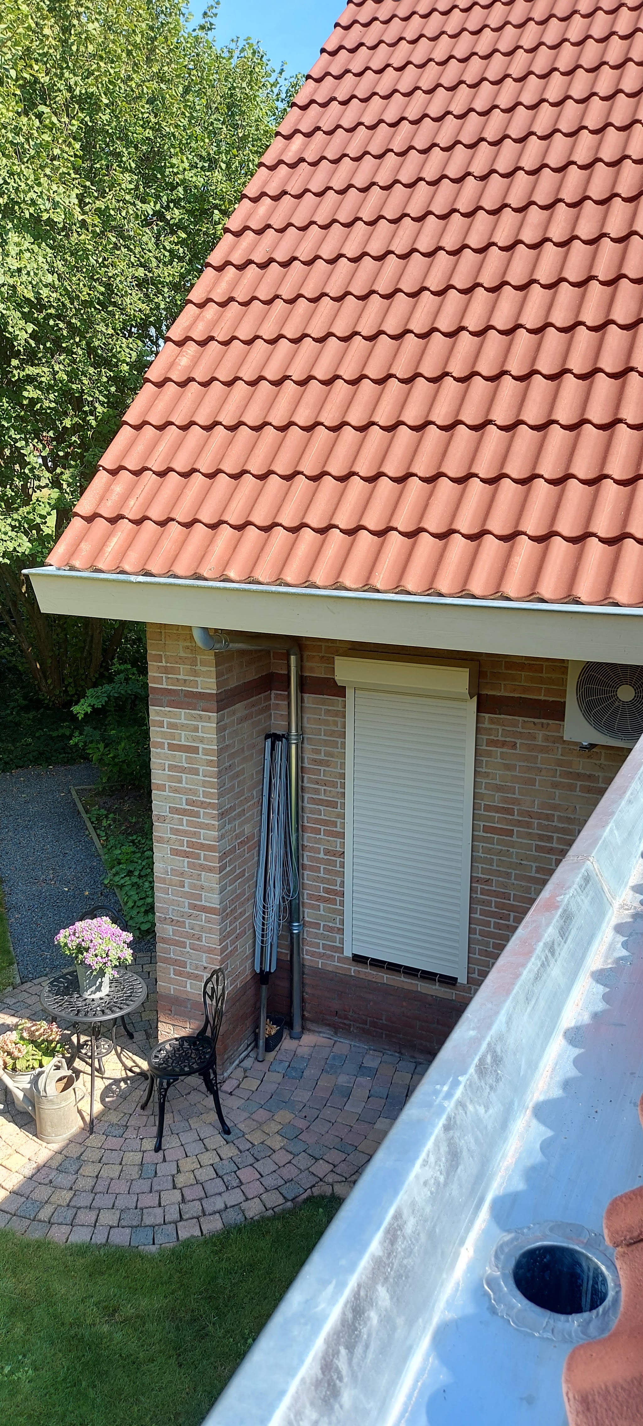 Nieuwe zinken goot met uitloop onder een oranje pannendak, tuin eronder