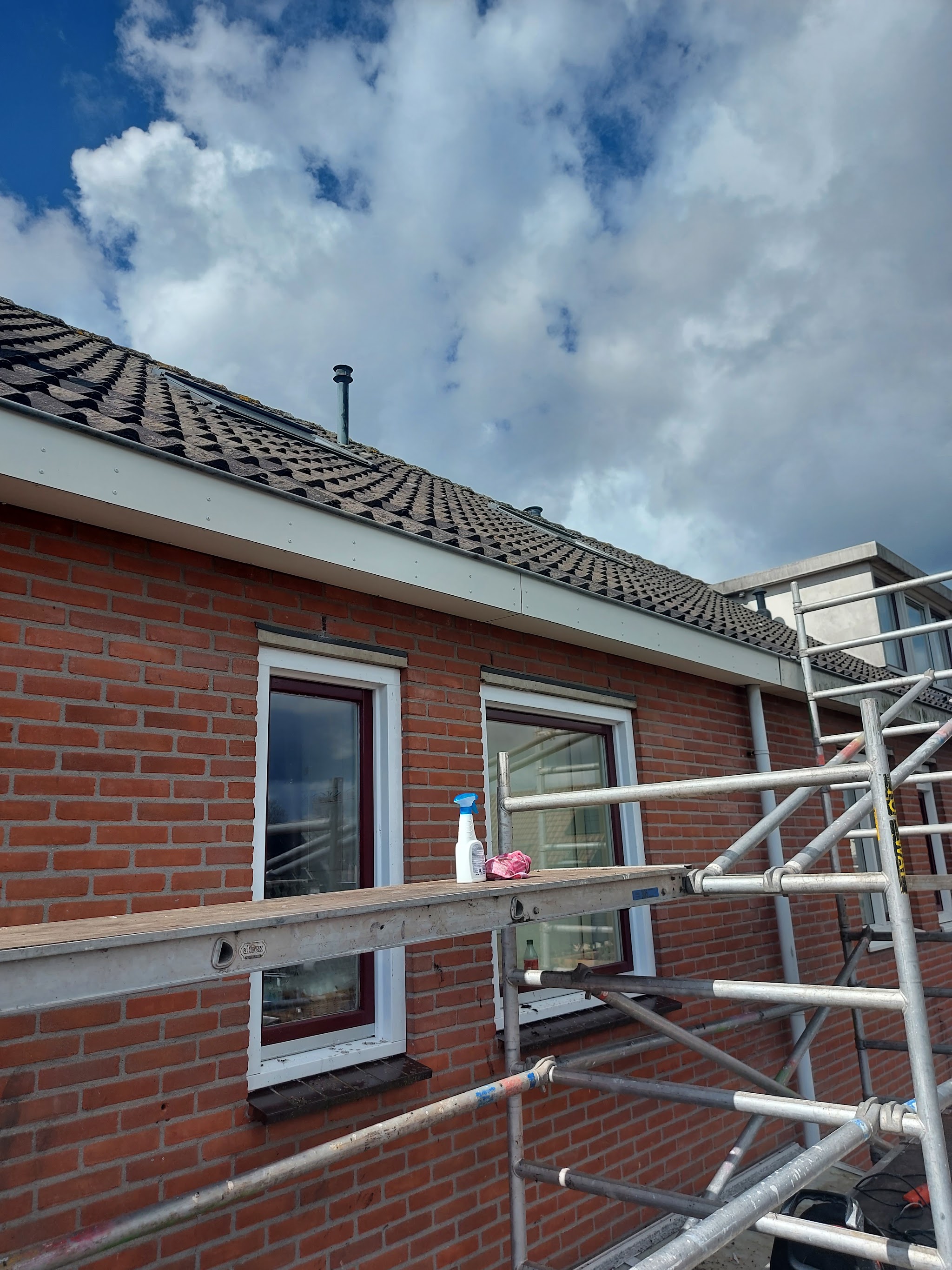 Steiger langs een bakstenen rijtjeshuis met een pannendak, blauwe lucht